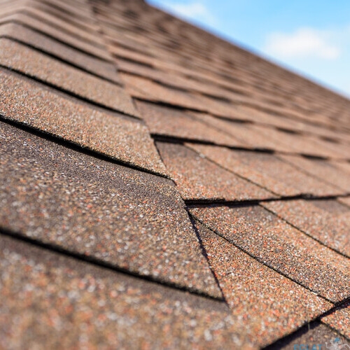 Close up and selective focus photo of asphalt shingle or tile on roof of new house under construction against blue sky