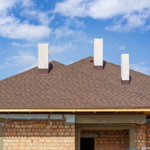 Asphalt tile roof with three white and new chimney on install on residential house under construction against blue background