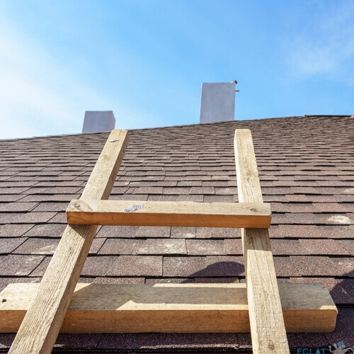 Photo of asphalt shingles or tile roof with wooden and safety ladder on new home under construction against beautiful blue sky