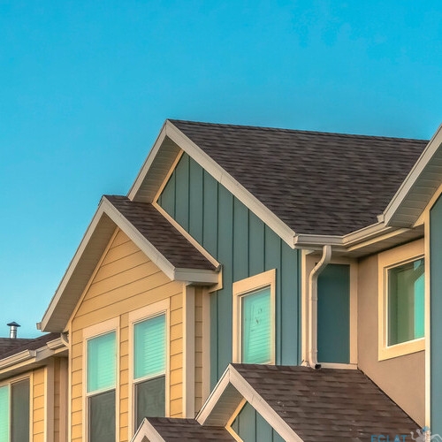 Panorama frame Exterior of upper storey of townhomes with blue sky background on a sunny day. The townhouses have pitched roofs, square windows, and blue and cream wall.