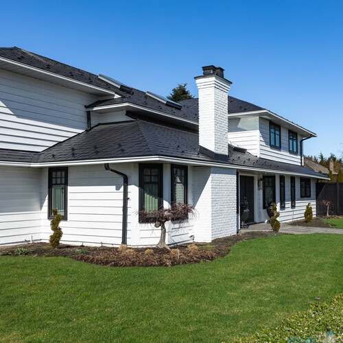 Real Estate Exterior Front House on a sunny day. Big custom made luxury house with nicely landscaped front yard in the suburbs. Luxurious big beautiful house. Spacious family home with green lawn in front