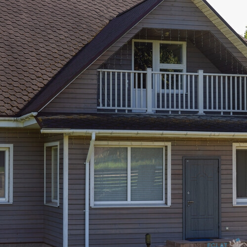 Residential house with porch lawn and wooden structures under clear blue sky. Well maintained countryside home with porch carport and wooden annex ideal for real estate architecture lifestyle.