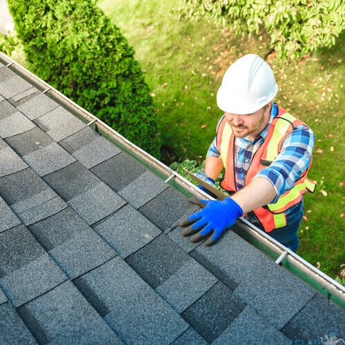 A man with hard hat standing on steps inspecting house roof