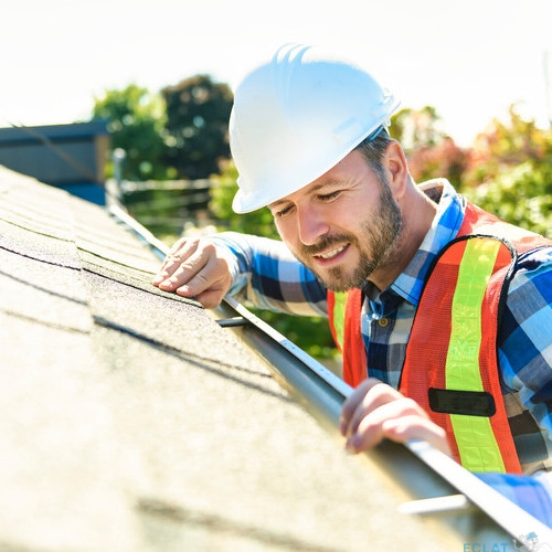 A man with hard hat standing on steps inspecting house roof