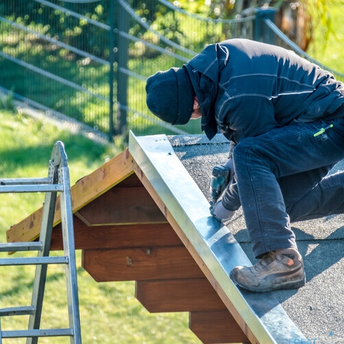 Roofer worker using battery-powered screw gun to fix metal facing