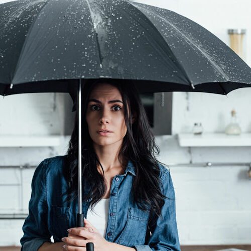 A Scared Woman Stands Underneath an Umbrella During a Roof Leak